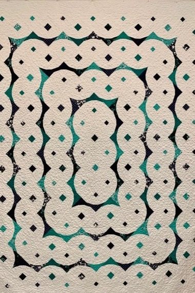 Quilt Title: Magic Potion. A white quilt with a blue and teal pattern of circles and squares, where the circlesmake and interconnected border of progressively smaller shapes. Quilter: Sandra Bonomo from Milk and Honey Guild.